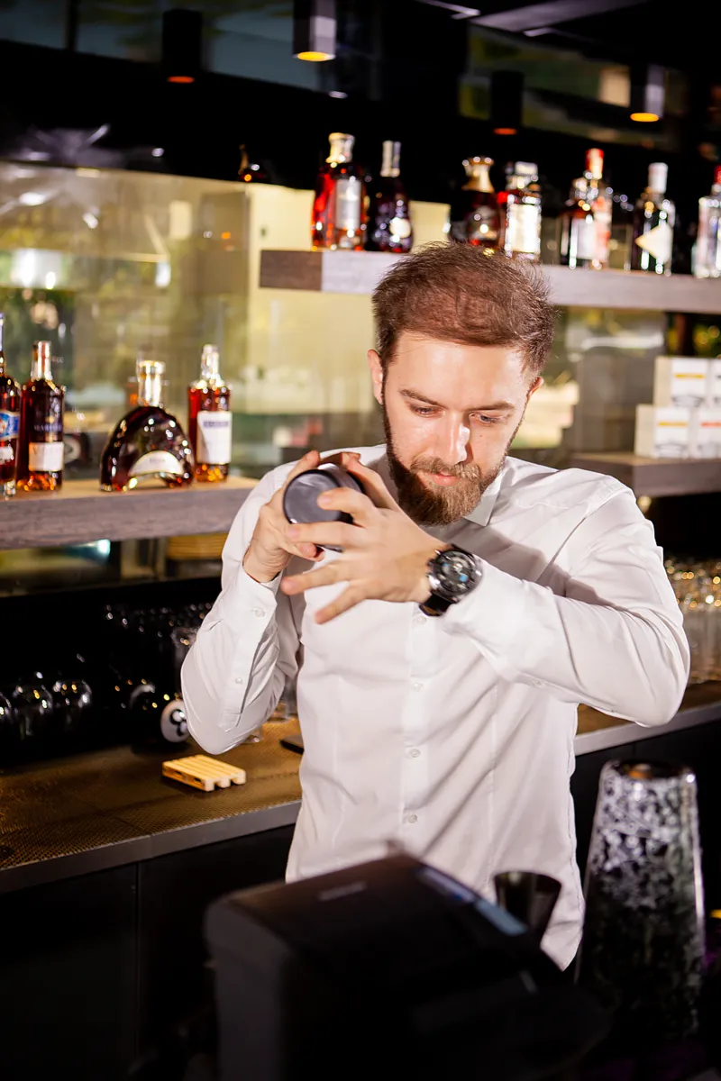 A bartender shaking a cocktail behind a lit back bar