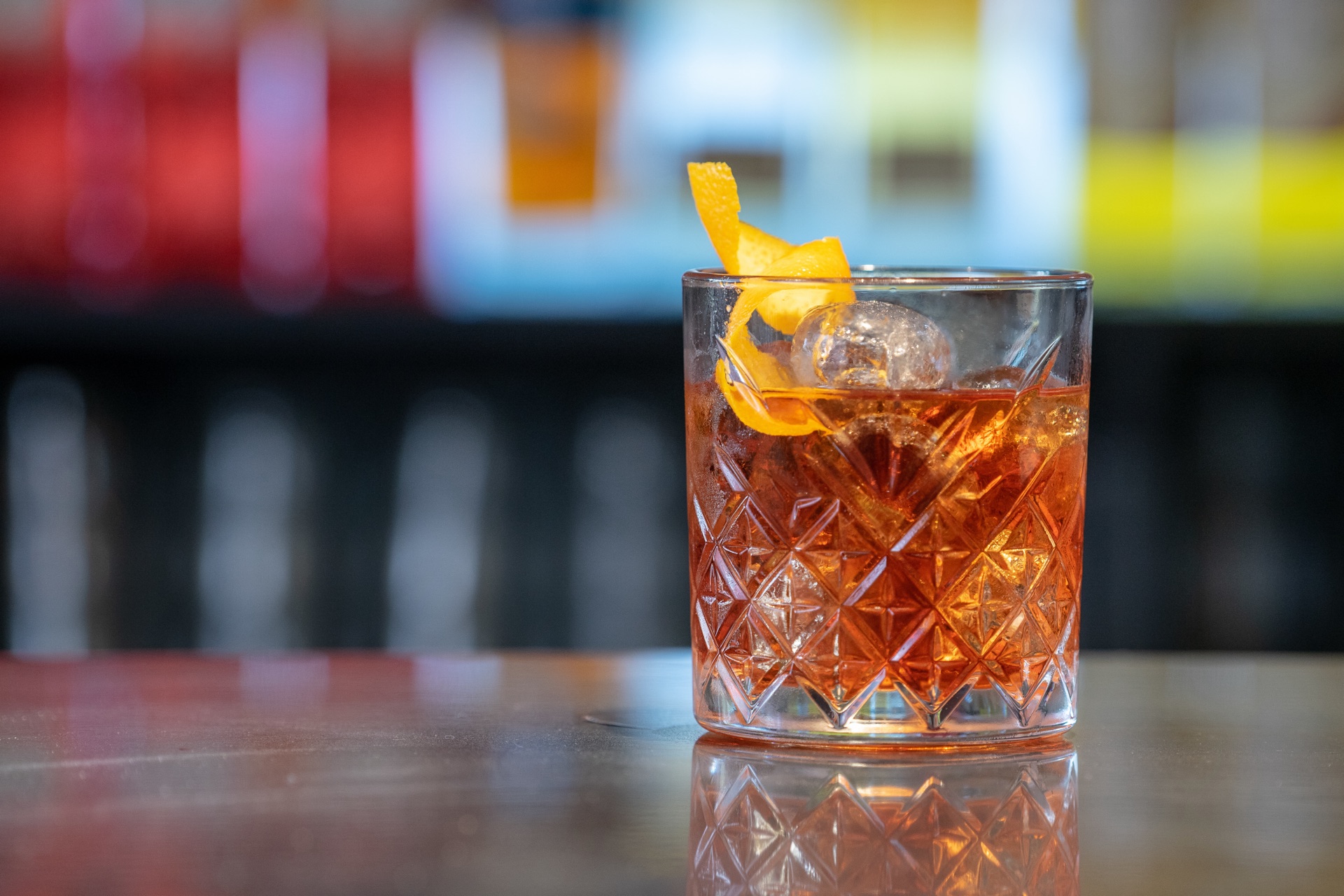 A Negroni in a cut-crystal rocks glass over a large ice cube, with an orange twist
